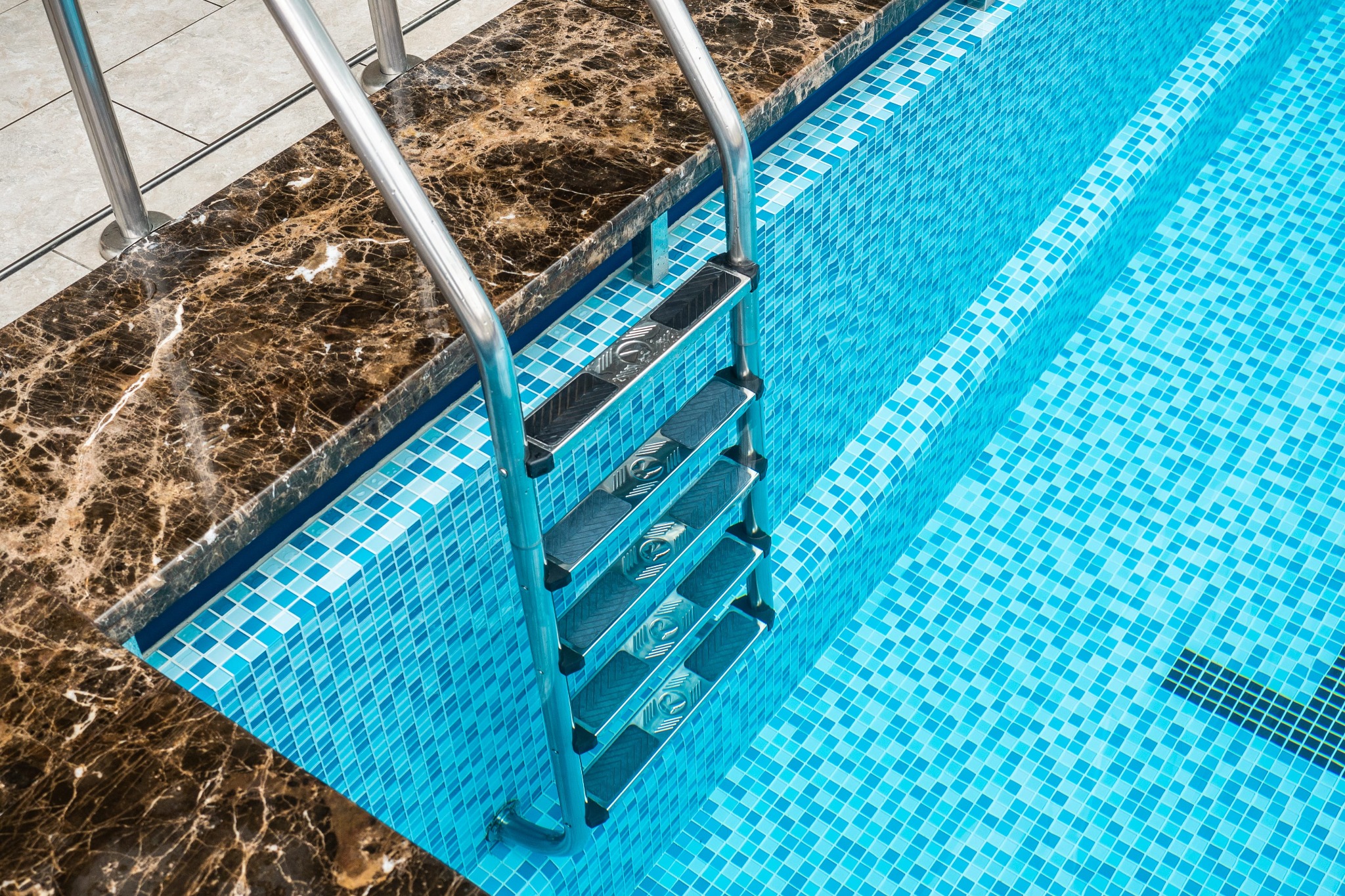 Stainless steel ladder beside a blue tiled swimming pool